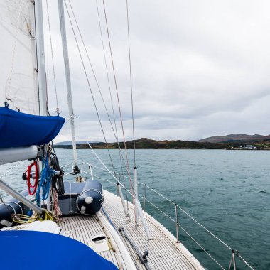 Bulutlu bir günde, Jura adasının kayalık kıyılarında seyir halindeki ahşap meşe güvertesiyle donatılmış modern bir yat. Inner Hebrides, İskoçya, İngiltere. Spor, eğlence, gezi, seyahat yerleri.