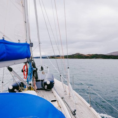 Bulutlu bir günde, Jura adasının kayalık kıyılarında seyir halindeki ahşap meşe güvertesiyle donatılmış modern bir yat. Inner Hebrides, İskoçya, İngiltere. Spor, eğlence, gezi, seyahat yerleri.