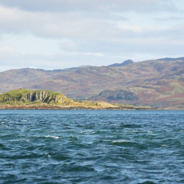 Jura adasının kıyılarının panoramik manzarası, dağları ve vadileri sudan. Bulutlu mavi gökyüzü. Paps of Jura, Inner Hebrides, İskoçya, İngiltere