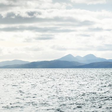 Jura adasının kıyılarının panoramik manzarası, dağları ve vadileri sudan. Bulutlu mavi gökyüzü. Paps of Jura, Inner Hebrides, İskoçya, İngiltere