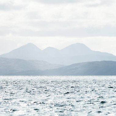 Jura adasının kıyılarının panoramik manzarası, dağları ve vadileri sudan. Bulutlu mavi gökyüzü. Paps of Jura, Inner Hebrides, İskoçya, İngiltere