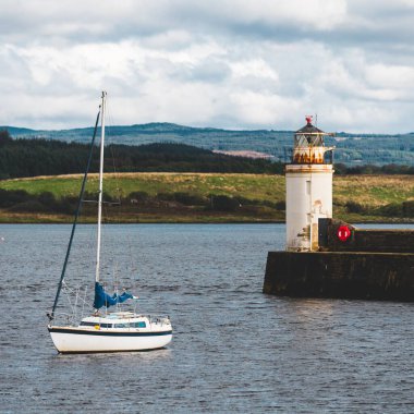 Bulutlu bir günde yelken açan küçük bir yat, yakın plan. Arka planda kayalık kıyılar var. Dramatik bulut manzarası. Ardrishaig, Crinan Kanalı, İskoçya, İngiltere. Seyahat yerleri, spor, eğlence.