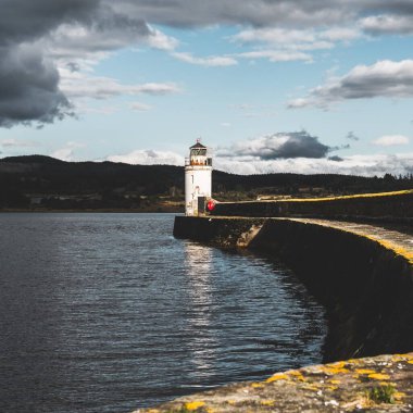 Eski deniz fenerine doğru boş bir gezinti, yakın plan. Arka planda kayalık kıyılar var. Dramatik bulut manzarası. Ardrishaig, Crinan Kanalı, İskoçya, İngiltere. Seyahat yerleri, gezi teması