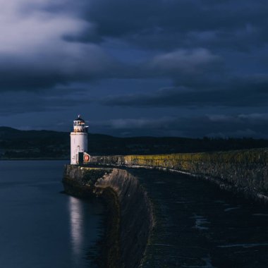 Gece eski deniz fenerine boş bir gezinti, yakın plan. Arka planda kayalık kıyılar var. Dramatik bulut manzarası. Ardrishaig, Crinan Kanalı, İskoçya, İngiltere. Seyahat yerleri, gezi teması