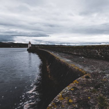 Eski deniz fenerine doğru boş bir gezinti, yakın plan. Arka planda kayalık kıyılar var. Dramatik bulut manzarası. Ardrishaig, Crinan Kanalı, İskoçya, İngiltere. Seyahat yerleri, gezi teması