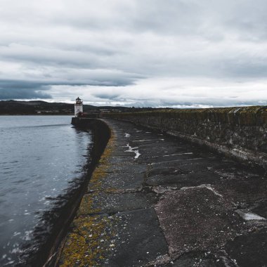 Eski deniz fenerine doğru boş bir gezinti, yakın plan. Arka planda kayalık kıyılar var. Dramatik bulut manzarası. Ardrishaig, Crinan Kanalı, İskoçya, İngiltere. Seyahat yerleri, gezi teması