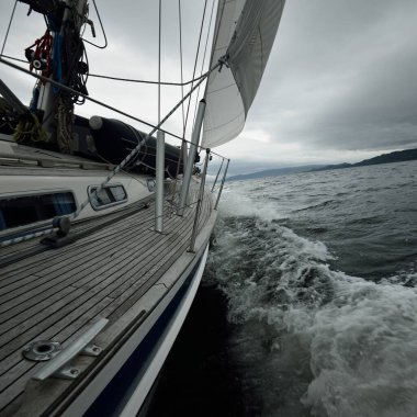 Bulutlu bir günde ahşap meşe güverteli, yelkenli, modern bir yat. Direğe ve yelkenlere bir manzara. Su, yakından sıçrıyor. Tarbert, İskoçya, İngiltere