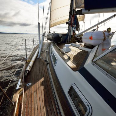 Bulutlu bir günde ahşap meşe güverteli, yelkenli, modern bir yat. Direğe ve yelkenlere bir manzara. Su, yakından sıçrıyor. Tarbert, İskoçya, İngiltere