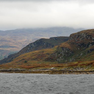 Bute 'un kayalık kıyılarının sudan panoramik görüntüsü. Tepeler ve dağlar arka planda. Karanlık fırtına gökyüzü. Bute Adası, Clyde Firth, İskoçya, İngiltere
