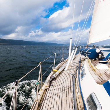 Teknelerle donatılmış modern bir yat. Tahta meşe güverteli. Clyde Nehri Firth 'ün kayalık kıyılarına doğru yol alıyorlar. Dramatik bir gökyüzü. İskoçya, İngiltere. Seyahat yerleri, eko turizm, tatiller, saf doğa.