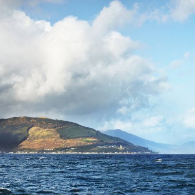 Sudan kayalık nehir kıyılarının panoramik görüntüsü. Arka planda ağaçlar, tepeler ve dağlar var. Bulutlu mavi gökyüzü. Gare Loch, Clyde Firth, İskoçya, İngiltere
