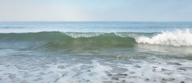 Güneş doğarken sisli bir havada Baltık Denizi kıyısından panoramik manzara. Dalgalar, sıçramalar, su yüzeyi. Yumuşak güneş ışığı, açık mavi gökyüzü. Idyllic yaz deniz manzarası. Saf doğa, çevre, ekoloji, eko-turizm