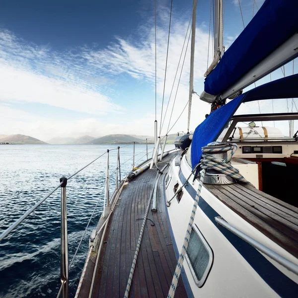 Storm sky. Sloop rigged modern yacht with wooden teak deck sailing  in the Firth of Clyde. Forests, hills and mountains of the Bute Island in the background. Scotland, UK