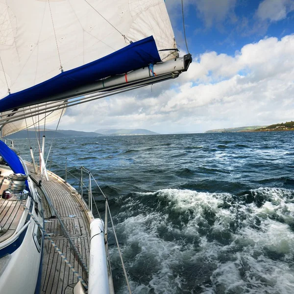 Sloop rigged modern yacht with wooden teak deck sailing on a cloudy day. A view to the mast and sails. Gare Loch, Firth of Clyde, Scotland, UK