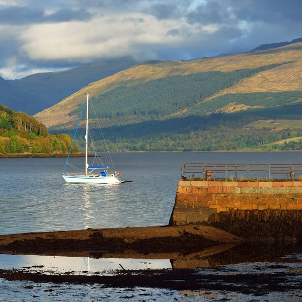 Loch Fyne yakınlarındaki sahil, orman ve tepelerin manzarası. Beyaz yelkenli yatla yakın plan. Inveraray, Inner Hebrides, Argyll ve Bute, İskoçya, İngiltere