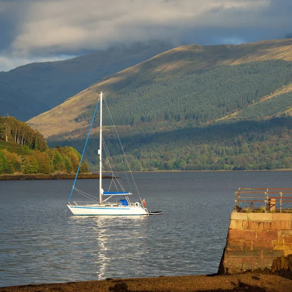 Loch Fyne yakınlarındaki sahil, orman ve tepelerin manzarası. Beyaz yelkenli yatla yakın plan. Inveraray, Inner Hebrides, Argyll ve Bute, İskoçya, İngiltere