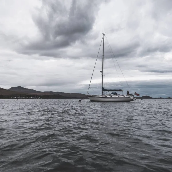 Yacht anchored on mooring near the rocky shore of Jura island under the stormy sky. Inner Hebrides, Scotland, UK. Travel destinations, landmarks, transportation, recreation, leisure activity