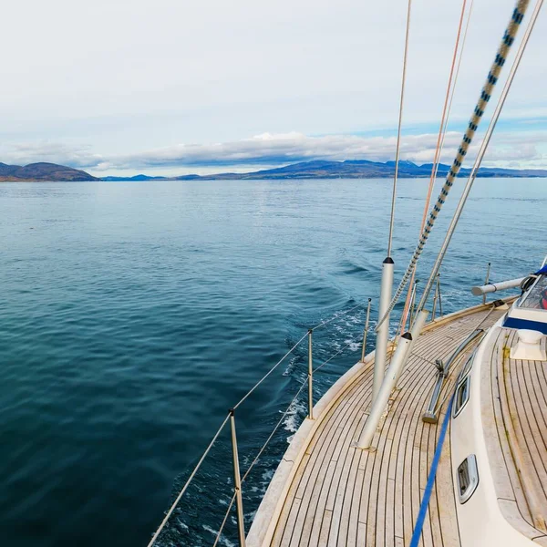 Bulutlu bir günde, Jura adasının kayalık kıyılarında seyir halindeki ahşap meşe güvertesiyle donatılmış modern bir yat. Inner Hebrides, İskoçya, İngiltere. Spor, eğlence, gezi, seyahat yerleri.