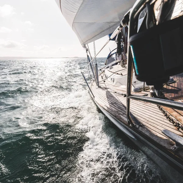 Sloop rigged modern yacht with wooden teak deck racing through the waves. A view from the deck to the bow. Water splashes close-up. Isle of Islay, Inner Hebrides, Scotland, UK. Sport and recreation