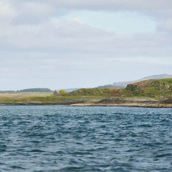 Jura adasının kıyılarının panoramik manzarası, dağları ve vadileri sudan. Bulutlu mavi gökyüzü. Paps of Jura, Inner Hebrides, İskoçya, İngiltere