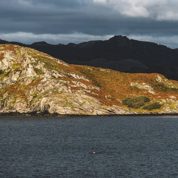 Kayalık kıyılar, kayalıklar, dağ tepeleri, Crinan ormanları ve tepeleri, bir yelkenli teknesinin manzarası. Argyll ve Bute, İskoçya, İngiltere. Panoramik manzara. Dramatik bir gökyüzü. Seyahat yerleri, eko turizm