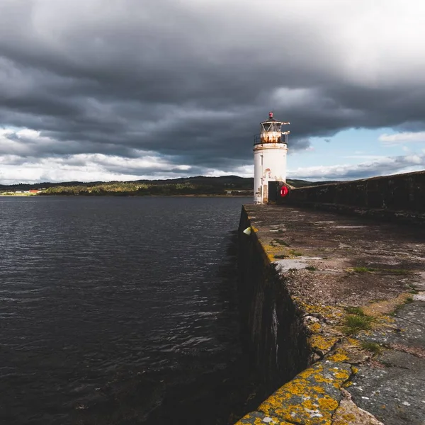 Eski deniz fenerine doğru boş bir gezinti, yakın plan. Arka planda kayalık kıyılar var. Dramatik bulut manzarası. Ardrishaig, Crinan Kanalı, İskoçya, İngiltere. Seyahat yerleri, gezi teması