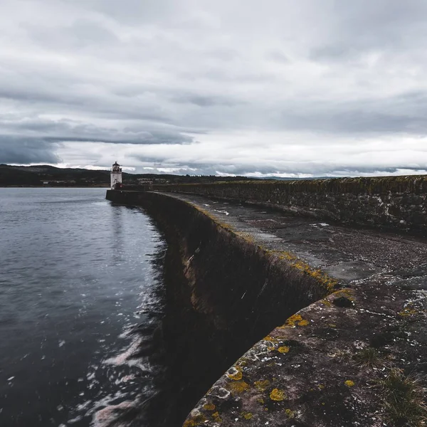 Eski deniz fenerine doğru boş bir gezinti, yakın plan. Arka planda kayalık kıyılar var. Dramatik bulut manzarası. Ardrishaig, Crinan Kanalı, İskoçya, İngiltere. Seyahat yerleri, gezi teması