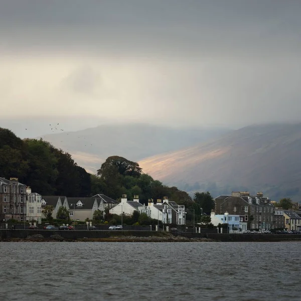 暴风雨的天空从水面俯瞰一个小镇的全景 乡村住宅和汽车的特写镜头 山丘和山脉在后面 Bute Island Firth Clyde Scotland — 图库照片