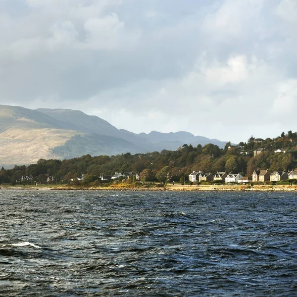 从水面俯瞰岩石河岸的全景 乡间别墅 小山和山峦在后面 多云的蓝天 Gare Loch Firth Clyde Scotland — 图库照片