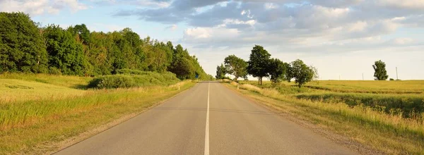Gün batımında tarım arazisi ve ormanın içinden geçen şehir otoyolu. Fırtınadan sonra dramatik bir gökyüzü. Sonbaharın başında. Yumuşak akşam güneşi. Tatiller, yol gezisi, sürüş, yolculuk