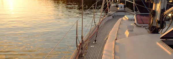 Old classic sailboat with wooden teak deck moored to a pier in a yacht marina at sunset. Vacations, transportation, sport, recreation, tourism, cruise, port service