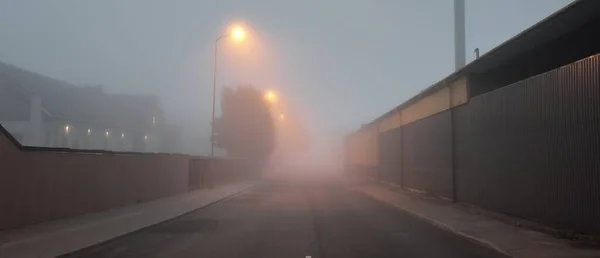 霧の中で近代的な工業ビルの近くに照明アスファルトの道路 街灯だ 街の風景 暗い都会の風景 インフラ 生態系の概念 — ストック写真