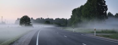 Boş bir otoyol (yeni asfalt yol) gün batımında sisli bir havada tarlalar ve ormanlar arasında. Yumuşak güneş ışığı. Kırsal alan. Uzak yerler, köy, yol gezisi, turizm, rota, lojistik, özgürlük kavramları