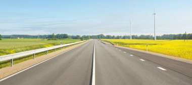 Gün doğumunda çiçek açan kolza tohumu tarlasında ve ormanda otoyol. Rüzgar türbini jeneratörleri (çiftlik). Ulaşım, eko-turizm, ekoloji, yenilenebilir enerji, teknoloji, altyapı, doğada güç