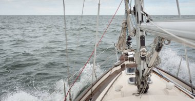 Fırtınada açık denizde yelken açan eski klasik bir yat. Tahta meşe güvertesi. Ketçap yelkenli. Dalgalar, su sıçramaları. Gezi, tatil, yelkenli yarışı, spor, boş zaman aktivitesi.