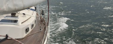 Fırtınada açık denizde yelken açan eski klasik bir yat. Tahta meşe güvertesi. Ketçap yelkenli. Dalgalar, su sıçramaları. Gezi, tatil, yelkenli yarışı, spor, boş zaman aktivitesi.