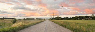Tarlaların ve ormanların arasından geçen bir köy yolu. Dramatik gökyüzü, parlayan bulutlar. Yerel turizm, yol gezisi, altyapı, ücra yerler, köy, çiftlik. Idyllic kırsal alanı