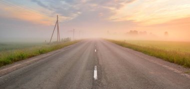 Kırsal karayolu (eski asfalt yolu) gün doğumunda tarla ve ormanın içinden geçer. Yumuşak güneş ışığı, parlayan pembe ve altın bulutlar. Elektrik hattı, trafo direkleri, kablolar. Tatiller, lojistik