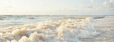 Fırtınadan sonra Baltık kıyıları. Gün batımı, yumuşak altın güneş ışığı. Su yüzeyi dokusu, çarpan dalgalar ve sıçramalar, köpük. Resimli panoramik manzara. Idyllic deniz manzarası. Doğa, çevre, ekoloji