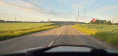 Gündoğumunda tarla ve ormanın içinden (asfalt yol) geçer. Yumuşak güneş ışığı, parlayan bulutlar. Tatiller, lojistik, ücra yerler. Arabadan bak.