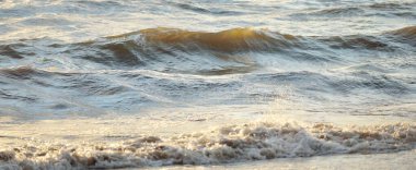 Fırtınadan sonra Baltık kıyıları. Gün batımı, yumuşak güneş ışığı. Su yüzeyi dokusu, çarpan dalgalar ve sıçramalar, köpük. Resimli panoramik manzara, arka plan. Doğa, çevre, ekoloji kavramları