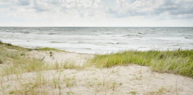 Fırtınadan sonra Baltık kıyıları (kum tepeleri, plaj). Dramatik gökyüzü, parlayan bulutlar. Resimli panoramik manzara. Doğa, çevre, ekoloji, eko-turizm, yürüyüş, keşif kavramları