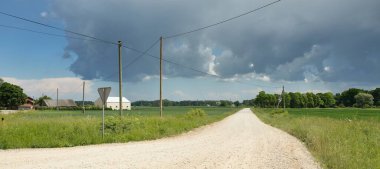Fırtınadan sonra tarladan geçen boş köy yolu. Arabadan bir manzara. Idyllic kırsal kesim. Renkli, parlayan günbatımı bulutları. Ulaşım, yolculuk, özgürlük, seyahat tutkusu, uzak yerler kavramları.