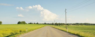 Tarımsal alan ve ormanın içinden geçen ülke otoyolu. Fırtınadan sonra dramatik bir gökyüzü. Yazın kırsal alanda. Yumuşak güneş ışığı. Tatiller, yol gezisi, sürüş, yolculuk
