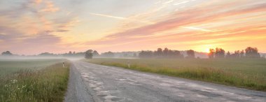 Kırsal karayolu (eski asfalt yolu) gün doğumunda tarla ve ormanın içinden geçer. Yumuşak güneş ışığı, parlayan pembe ve altın bulutlar. Tatiller, lojistik, uzak yerler