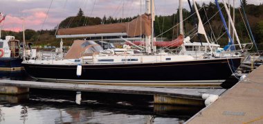 Günbatımında yat limanında demirlemiş zarif ve modern yelkenliler. Dramatik bulutlar. Inner Hebrides, İskoçya, İngiltere. Ulaşım, spor, yelkencilik, eğlence, eğlence, eğlence, gezi, turizm