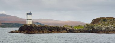 Rocky gölü kıyıları, dağ zirveleri, dağlar, vadiler ve tepeler. Deniz feneri. Yelkenliden panoramik manzara. Dramatik bir gökyüzü. İskoçya, İngiltere. Atmosferik manzara. Seyahat yerleri, yürüyüş, eko-turizm