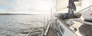 Kayalık göl kıyılarında seyir halindeki ahşap meşe güvertesiyle donatılmış modern bir yat. İskoçya, İngiltere. Güverteden pruvaya, direğe, yelkenlere bakın. Seyahat tutkusu, eğlence aktivitesi, spor, yelkenli yarışı, deniz yolculuğu.