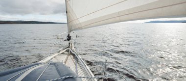 Kayalık göl kıyılarında seyir halindeki ahşap meşe güvertesiyle donatılmış modern bir yat. İskoçya, İngiltere. Güverteden pruvaya, direğe, yelkenlere bakın. Seyahat tutkusu, eğlence aktivitesi, spor, yelkenli yarışı, deniz yolculuğu.