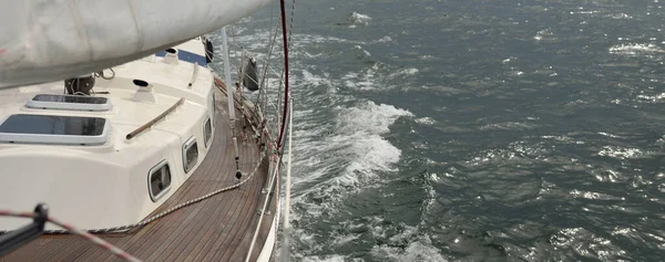 Fırtınada açık denizde yelken açan eski klasik bir yat. Tahta meşe güvertesi. Ketçap yelkenli. Dalgalar, su sıçramaları. Gezi, tatil, yelkenli yarışı, spor, boş zaman aktivitesi.